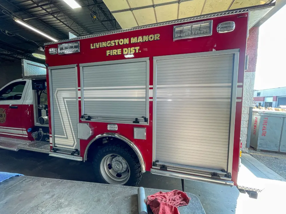 Exterior view of small fire truck showing cab, body compartments, and wheel/tire area.